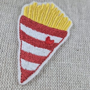 May include: Embroidered patch in the shape of a french fry container. The top is yellow, representing fries, and the bottom is red and white striped. A small red heart is embroidered on the front.