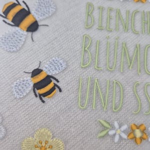 May include: A white fabric with embroidered bees, flowers, and the text "Bienchen Bl&uuml;mchen und Sonnenschein".