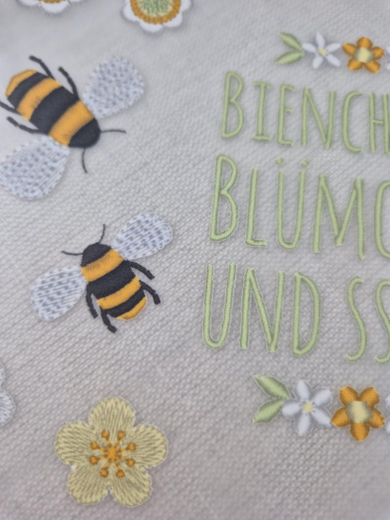 May include: A white fabric with embroidered bees, flowers, and the text "Bienchen Bl&uuml;mchen und Sonnenschein".