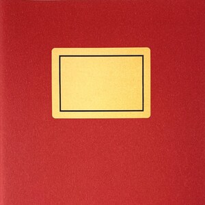 Op de afbeelding: Een rood notitieboek met een gouden rechthoek op de voorkant. De rechthoek heeft een zwarte rand.