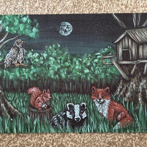 May include: A rectangular canvas painting depicts a nighttime forest scene with a full moon, a treehouse, and a bird perched on a branch. A squirrel sits on a stump, while a badger and a red fox are positioned in the green grass below.