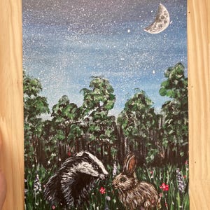 May include: A rectangular painting featuring a black and white badger and a brown rabbit standing in a field of green grass with small red and purple flowers. Behind them is a dense forest of green trees under a dark blue night sky with stars.