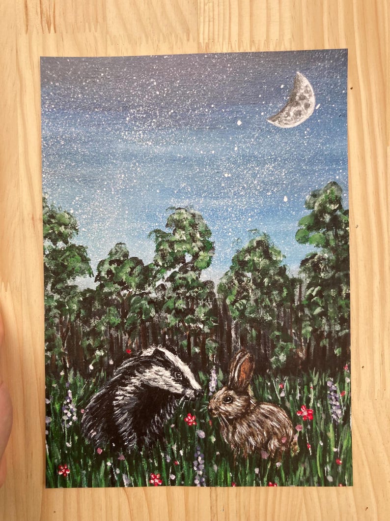 May include: A rectangular painting featuring a black and white badger and a brown rabbit standing in a field of green grass with small red and purple flowers. Behind them is a dense forest of green trees under a dark blue night sky with stars.