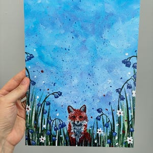 May include: A rectangular painting on canvas featuring a red fox centered at the bottom, surrounded by tall green grass, blue bell-shaped flowers, and small white blossoms against a textured, splattered light blue sky background.