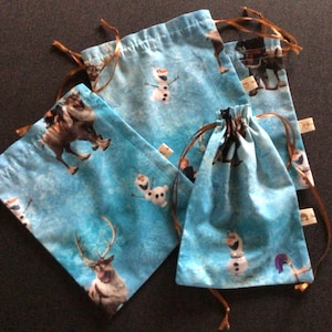 Könnte beinhalten: Vier blaue Stoffbeutel mit Kordelzug im Frozen-Design. Die Beutel zeigen Bilder von Olaf, Sven und Kristoff. Die Beutel haben braune Kordelzüge.