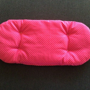 Könnte beinhalten: Ein rosa Babykissen mit weißen Punkten und einem kleinen weißen Etikett.