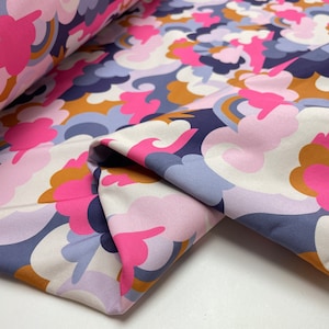 Op de afbeelding: Een stof met een herhalend patroon van roze, blauwe en bruine wolken op een witte achtergrond.