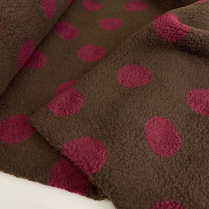 Könnte beinhalten: Ein brauner Fleece-Stoff mit einem sich wiederholenden Muster aus dunkelrosa kreisförmigen Punkten. Das Material hat eine dicke, strukturierte und flauschige Oberfläche mit weichem Aussehen, die Falten und Drapierungen zeigt.