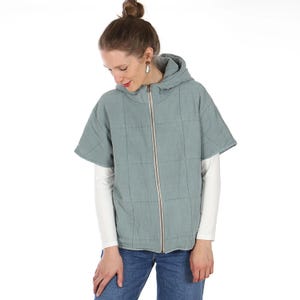 Op de afbeelding: Een lichtblauwe gewatteerde jas met capuchon en korte mouwen. De jas heeft een lange ritssluiting en wordt gedragen over een wit shirt met lange mouwen. Het model draagt een blauwe jeans.