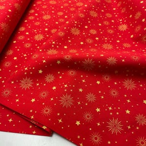 Peut inclure: Tissu rouge avec un motif répété d'étoiles dorées et de motifs en forme d'éclats. Le tissu est plié, révélant la texture et les détails de l'impression. Idéal pour les projets festifs.