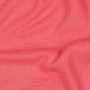 Op de afbeelding: Een close-up van een zachte, roze stof met een textuur. De stof is gekreukt en heeft een licht gekreukelde uitstraling.