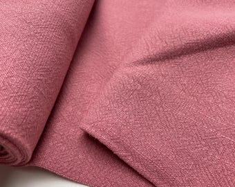 May include: Close-up of a roll of dusty rose-colored fabric. The fabric has a textured weave and appears to be linen or a similar material. The fabric is folded over itself, showing the texture and color variations.