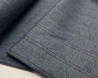 May include: Close-up of folded grey and blue fabric with a herringbone weave. Vertical stripes and subtle brown lines accent the material. The fabric appears to be a medium-weight suiting material, suitable for tailoring.