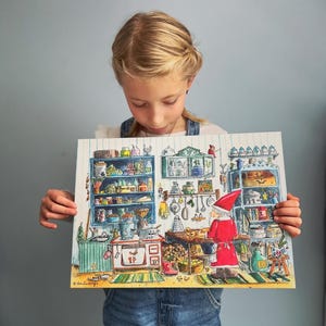 May include: A young girl holds up a colorful illustration of a kitchen scene with a gnome baking in front of a wood-burning stove. The illustration is filled with details, including shelves stocked with jars, pots, and pans.