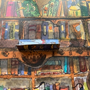 Op de afbeelding: Een close-up van een boekenplank met een klein, blauw en wit vogeltje op een plank. De plank is gemaakt van hout en heeft een bruine vlek. Het vogeltje houdt een klein, rood hartje in zijn bek. Het nummer "20" is zichtbaar op de plank.