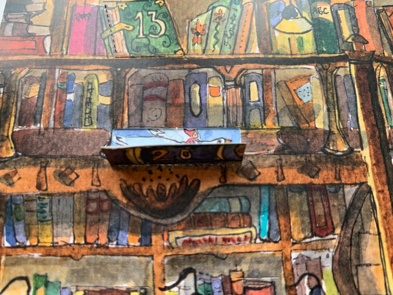 Op de afbeelding: Een close-up van een boekenplank met een klein, blauw en wit vogeltje op een plank. De plank is gemaakt van hout en heeft een bruine vlek. Het vogeltje houdt een klein, rood hartje in zijn bek. Het nummer "20" is zichtbaar op de plank.