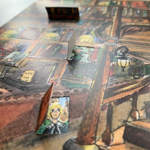 Op de afbeelding: Een aquarel-illustratie van een boekwinkelinterieur met een houten trap, planken vol boeken en een persoon die aan een bureau zit. De illustratie is gedrukt op een kaart met een uitsparing die een kleinere illustratie van een meisje met blond haar onthult.