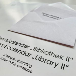 Op de afbeelding: Een witte envelop met de tekst "Adventskalender "Bibliothek II" - Advent calendar "Library II" L&ouml;sung im Umschlag solution in the envelope" erop gedrukt.