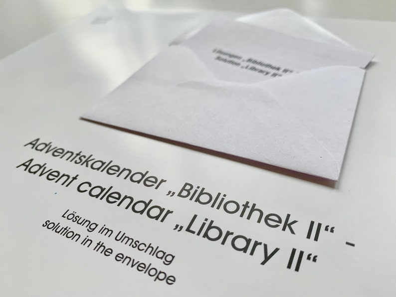 Op de afbeelding: Een witte envelop met de tekst "Adventskalender "Bibliothek II" - Advent calendar "Library II" L&ouml;sung im Umschlag solution in the envelope" erop gedrukt.
