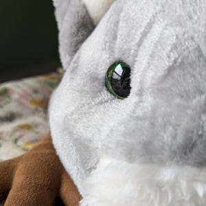May include: Close-up of a plush toy's eye. The eye is green with a black pupil and a reflective surface.