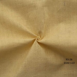 May include: A close-up of a pale yellow fabric with a textured weave. The fabric is folded and twisted, showing its drape and texture. The text "93-26 GSM-110" is printed in the bottom right corner.