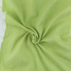 Pu&ograve; includere: Un pezzo di tessuto verde chiaro, piegato e stropicciato, che mostra la trama e il drappeggio del materiale.