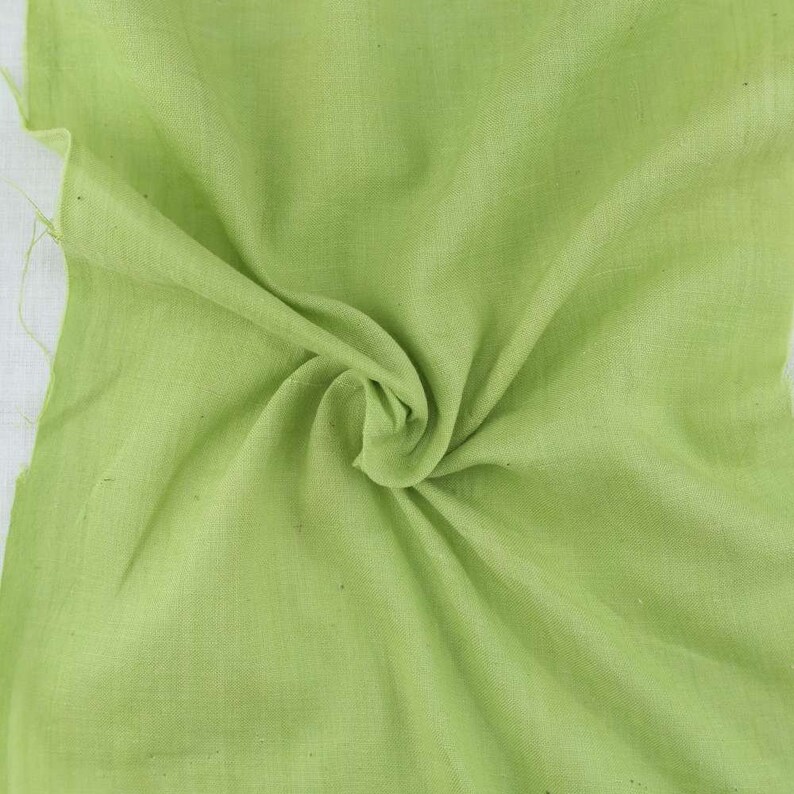 Pu&ograve; includere: Un pezzo di tessuto verde chiaro, piegato e stropicciato, che mostra la trama e il drappeggio del materiale.