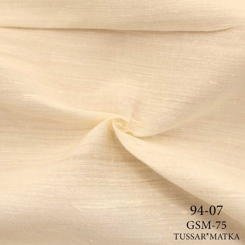May include: Close-up of a cream-colored fabric with a textured weave. The fabric is labeled "94-07 GSM-75 TUSSAR*MATKA".