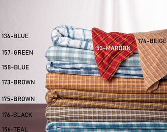 May include: A stack of eight plaid fabric swatches in various colors, including blue, green, brown, beige, maroon, black, and teal. The swatches are labeled with numbers and color names.