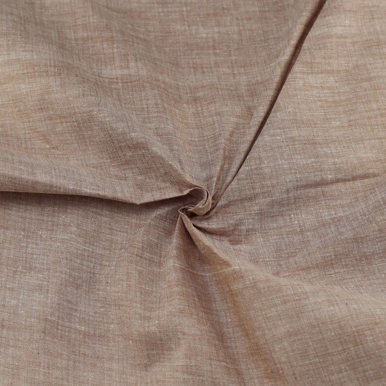 Op de afbeelding: Close-up van een bruine stof met een subtiele geweven textuur. De stof is gevouwen en gekreukt, waardoor de natuurlijke drape zichtbaar is.