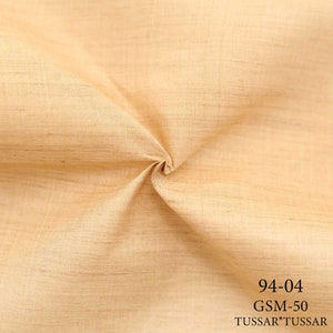 May include: A close-up of a beige fabric with a textured weave. The fabric is folded in the center and the text "94-04 GSM-50 TUSSAR*TUSSAR" is printed in black at the bottom.