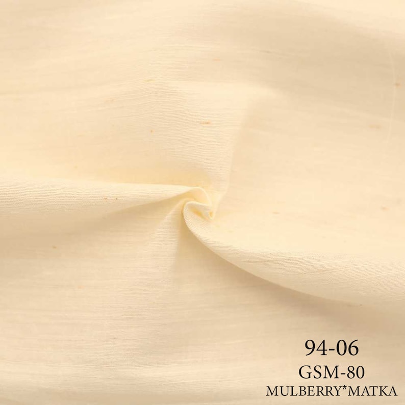 May include: Close-up of a cream-colored fabric with a slightly textured surface. The fabric is folded in the center and has a subtle sheen. The text "94-06 GSM-80 MULBERRY*MATKA" is printed in black at the bottom of the image.