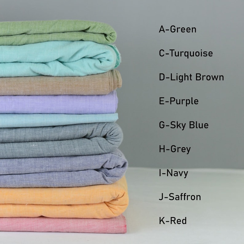 Op de afbeelding: Een stapel van tien stofstalen in verschillende kleuren, waaronder groen, turquoise, lichtbruin, paars, hemelsblauw, grijs, marineblauw, saffraan en rood. Elk staal is dubbelgevouwen en op elkaar gestapeld.