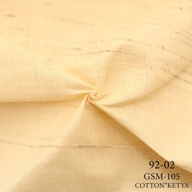 May include: Close-up of a pale yellow fabric with a subtle striped pattern. The fabric is folded and textured. The text "92-02 GSM-105 COTTON*KETYA" is printed in black at the bottom of the image.