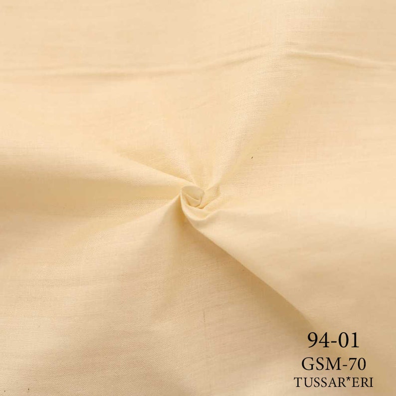 May include: A close-up of a smooth, off-white fabric with a slight sheen. The fabric is folded and has a slight wrinkle in the center. The text "94-01 GSM-70 TUSSAR*ERI" is printed in black at the bottom of the image.