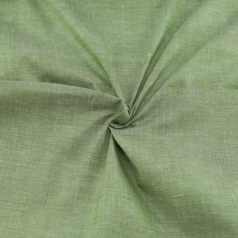 Op de afbeelding: Een close-up van een groene stof met een textuur. De stof is gevouwen en gedraaid, waardoor een draaiende vorm ontstaat.