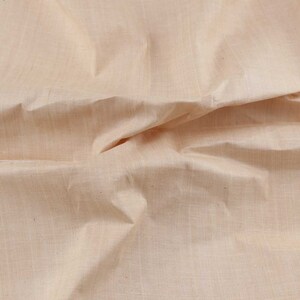 Pu&ograve; includere: Un primo piano di un tessuto liscio color beige chiaro con una texture sottile. Il tessuto &egrave; piegato e drappeggiato, mostrando la sua natura morbida e fluida.