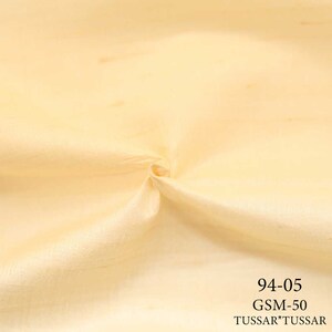 May include: A close-up of a pale yellow fabric with a smooth texture. The fabric is folded and has a slight sheen. The text "94-05 GSM-50 TUSSAR*TUSSAR" is printed in black at the bottom of the image.