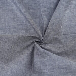 Op de afbeelding: Een close-up van een blauwe stof met een textuurweefsel. De stof is gevouwen en gekreukt, waardoor de textuur en de drape zichtbaar worden.