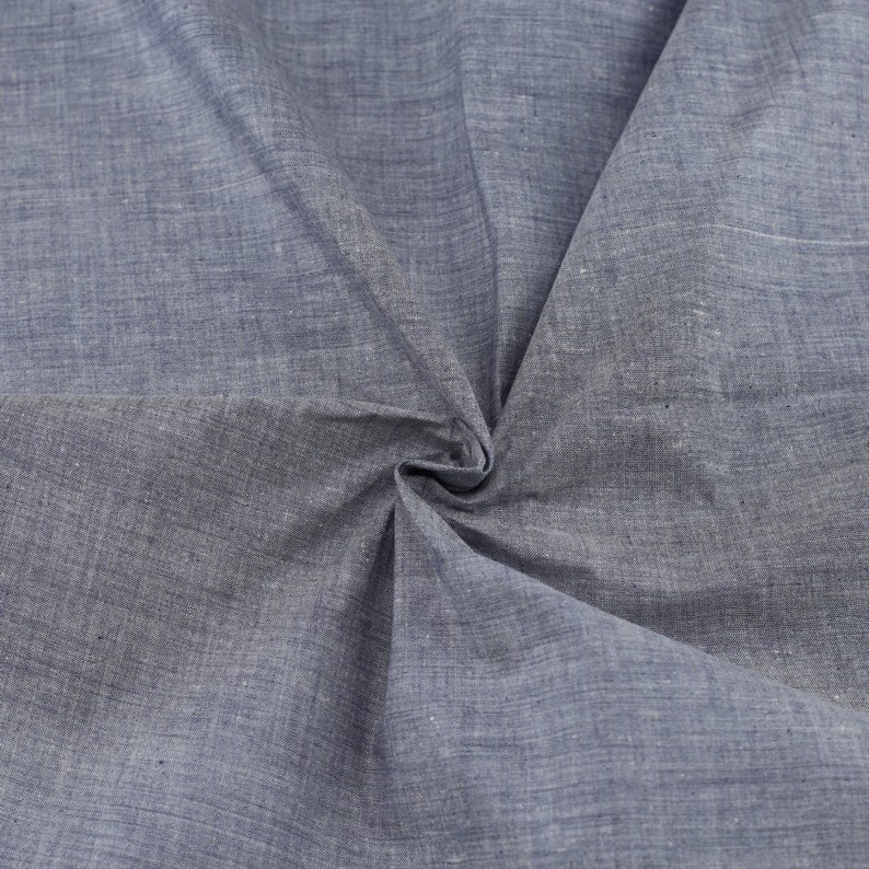 Op de afbeelding: Een close-up van een blauwe stof met een textuurweefsel. De stof is gevouwen en gekreukt, waardoor de textuur en de drape zichtbaar worden.