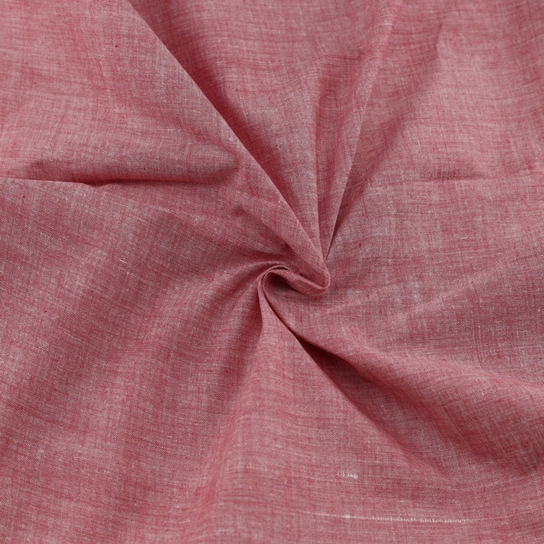 Op de afbeelding: Close-up van een zachte, rode stof met een subtiel textuurpatroon. De stof is gevouwen en gedrapeerd, waardoor de drape en textuur worden getoond.