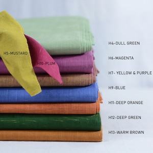 May include: A stack of fabric swatches in various colours, including mustard yellow, plum, dull green, magenta, yellow and purple, blue, deep orange, deep green, and warm brown. The swatches are labelled with their corresponding colour names.
