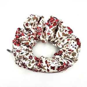 May include: A white scrunchie with a red and brown floral pattern. The scrunchie is made of fabric and has a gathered look.