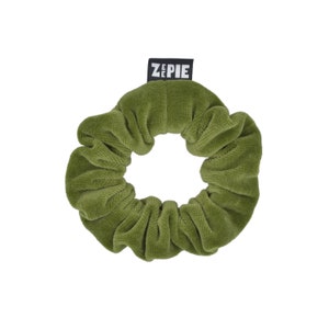 Könnte beinhalten: Ein grünes Samt-Haargummi mit dem Wort "ZEPIE" auf einem schwarzen Etikett.