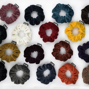 Könnte beinhalten: Sortiment von 15 Samt-Haargummis in verschiedenen Farben, darunter Burgunderrot, Schwarz, Weiß, Rot, Braun, Teal, Gelb, Marineblau, Grau und Orange. Jedes Haargummi hat ein kleines schwarzes Etikett mit dem aufgedruckten Wort "ZIPPIE".