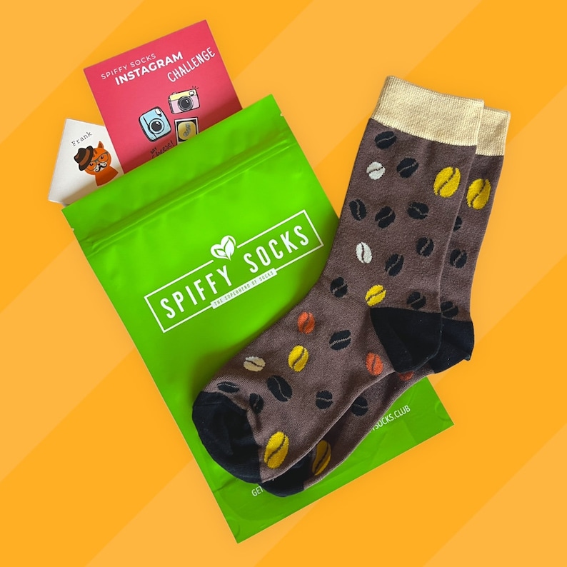 以下が含まれることがあります： コーヒー豆柄の茶色の靴下2足。靴下は「Spiffy Socks」と「The Supreme of Socks」の文字が書かれた緑色の袋に入っています。