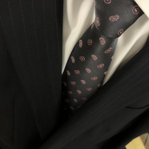 May include: A black suit jacket with a white dress shirt and a dark tie with a pink paisley pattern.