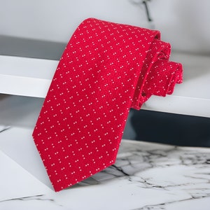 May include: A red tie with a white polka dot pattern. The tie is folded and lying on a white surface.