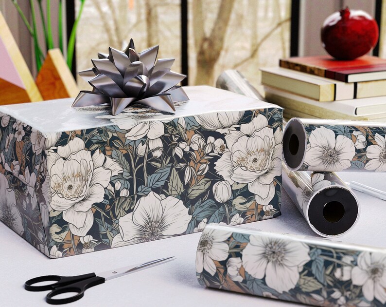 May include: A wrapped gift box with a silver bow, featuring floral patterned wrapping paper in white, navy, and tan. Rolls of matching wrapping paper and a pair of black scissors are also visible.