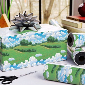 May include: A wrapped gift box with a silver bow, featuring landscape-themed wrapping paper with green hills, blue skies, and fluffy white clouds. Rolls of matching wrapping paper and a pair of black scissors are also visible.